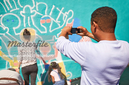 Man with camera phone photographing community mural on sunny wall