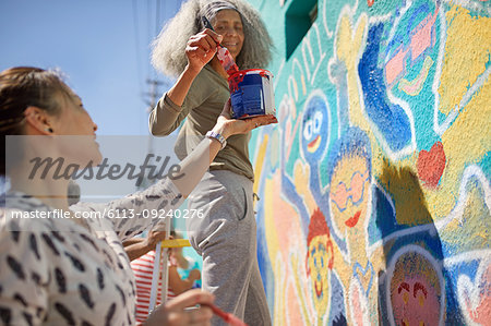 Female volunteers painting vibrant community mural on sunny urban wall