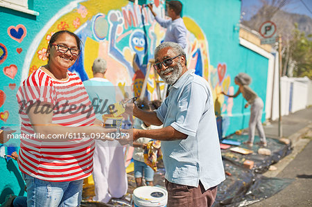 Portrait happy community volunteers painting mural on sunny urban wall