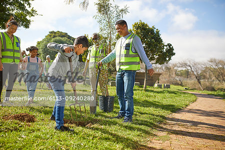 Multi-generation family volunteers planting trees in sunny park