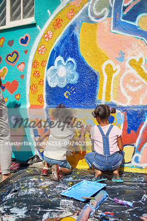 Girls painting vibrant mural on sunny wall