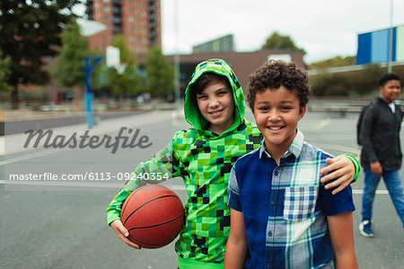 Portrait happy junior high boy friends playing basketball in schoolyard