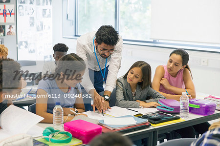 Male teacher helping junior high school girl students at desk in classroom