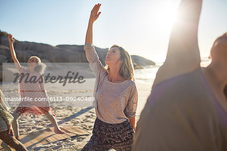 Serene woman practicing reverse warrior pose on sunny beach during yoga retreat