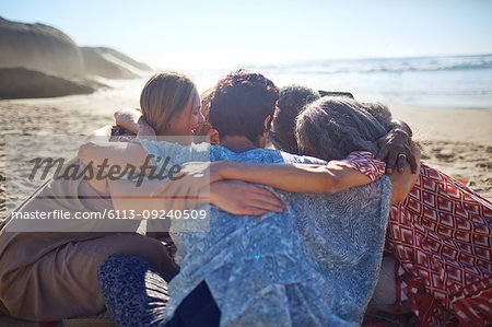 Group hugging in circle on sunny beach during yoga retreat