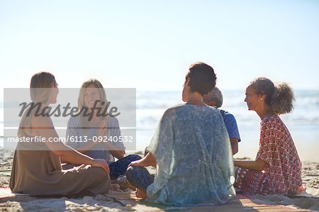 Happy friends talking in circle on sunny beach during yoga retreat
