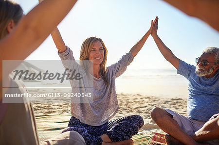 Happy friends joining hands in circle on sunny beach during yoga retreat