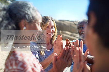 Friends with hands clasped in circle on sunny beach during yoga retreat