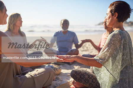 Serene people meditating in circle on sunny beach during yoga retreat