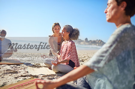 Serene women meditating on sunny beach during yoga retreat