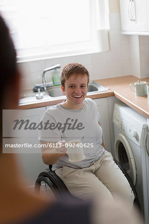 Smiling young woman in wheelchair drinking tea in apartment kitchen