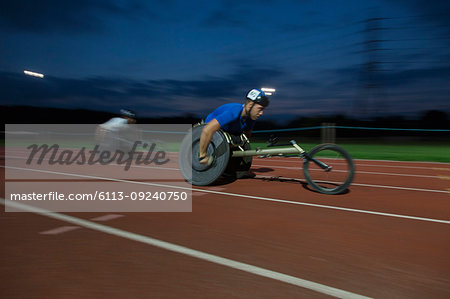 Determined young male paraplegic athlete speeding along sports track in wheelchair race at night