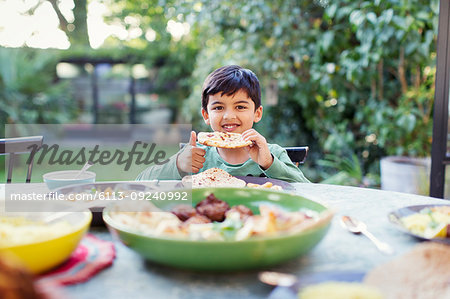 Portrait happy boy eating naan bread at patio table