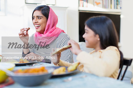 Happy mother in hijab and daughter eating dinner