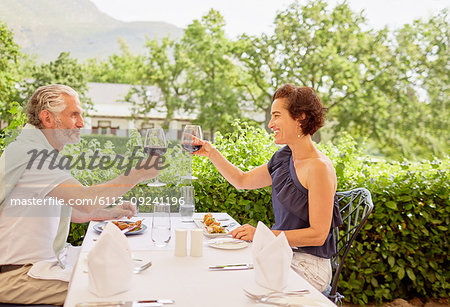 Mature couple toasting wine glasses at patio restaurant table