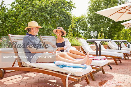 Mature couple relaxing on lounge chairs at sunny poolside