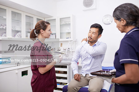 Male patient explaining shoulder pain to female doctor in clinic examination room
