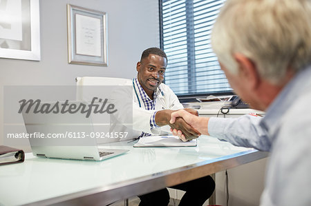 Male doctor shaking hands with senior patient in doctors office