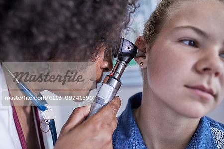 Close up female pediatrician using otoscope, examining ear of girl patient