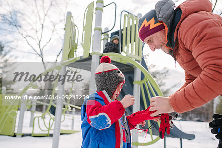 Father putting on boy's gloves by playground slide in snow