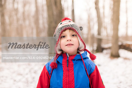 Boy in knit hat by snow covered forest, portrait