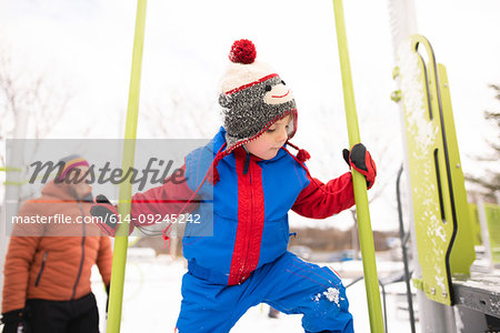 Boy with father climbing up playground slide in snow