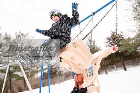 Boy jumping from playground swing in snow