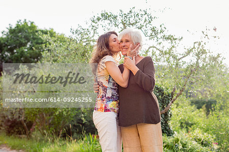 Mature woman kissing mother on cheek in garden