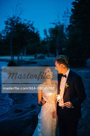 Romantic bride and groom with sparklers strolling on lakeside at dusk