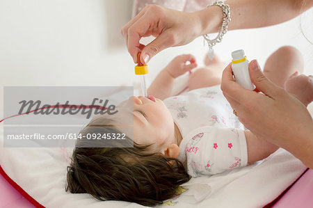 Mother feeding baby girl medicine in bed