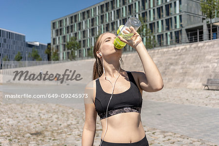 Young woman taking break from exercise and drinking water in city, Berlin, Germany