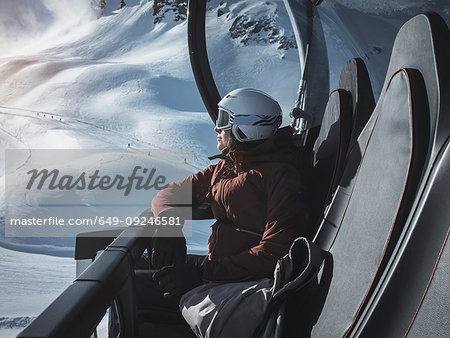 Young woman skier wearing helmet and ski goggles looking out from ski lift,  Alpe Ciamporino, Piemonte, Italy