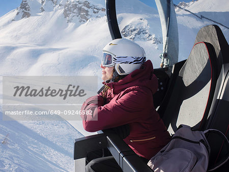 Young woman skier wearing helmet and ski goggles looking out from ski lift,  Alpe Ciamporino, Piemonte, Italy