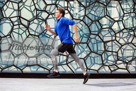 Young runner jogging past glass wall, London, UK