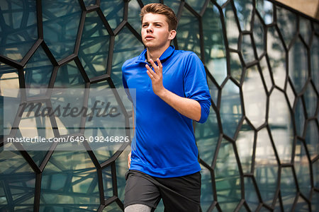 Young runner jogging past glass wall, London, UK