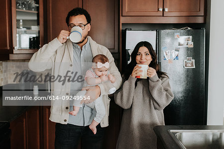 Couple having drink and carrying baby daughter in kitchen