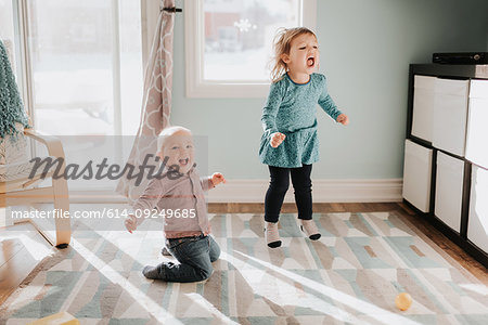 Female toddler and baby brother playing on living room rug