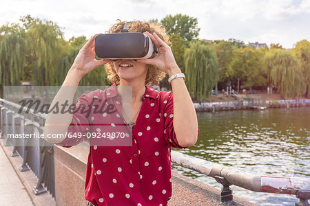 Young woman using VR headset on bridge, river in background, Berlin, Germany