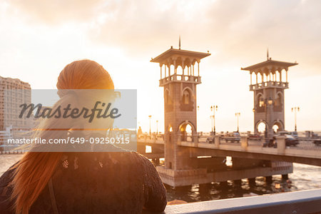 Female tourist with red hair looking out over Stanley bridge at sunset, rear view, Alexandria, Egypt