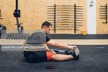 Man with prosthetic leg stretching on gym floor