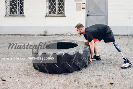 Man with prosthetic leg weight training with giant tyre