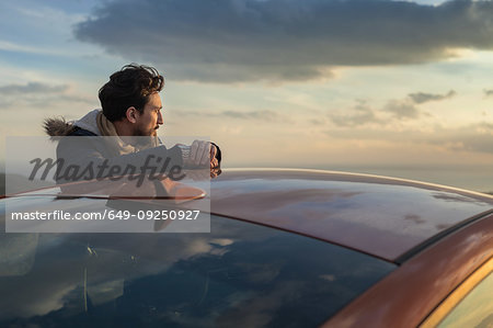 Man resting against car on roadside, enjoying view on hilltop