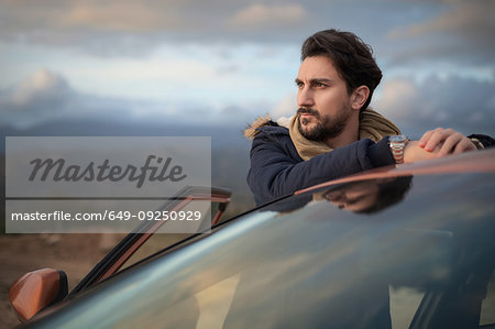 Man resting against car on roadside, enjoying view on hilltop