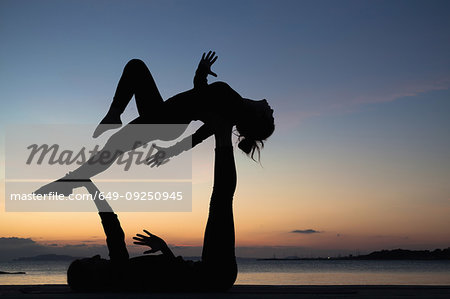 Women practising acro yoga at seaside