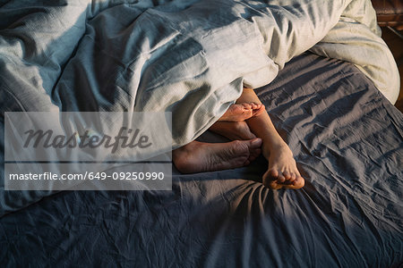 Couple's feet sticking out from under duvet in bed