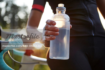 Female cyclist holding water bottle, mid section