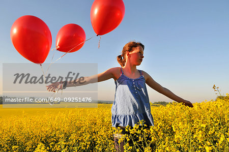 Girl with red balloons on rapeseed field, Eastbourne, East Sussex, United Kingdom