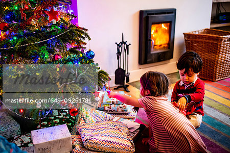 Girl and male toddler playing by living room christmas tree