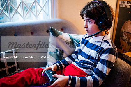 Boy sitting on sofa wearing headset and  using game controller