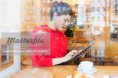 Mid adult woman in cafe using digital tablet touchscreen, window view